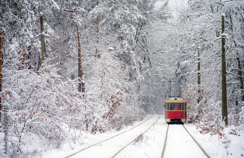 Old red tram, leaving the distance through the snow-covered forest. Back view. Selective focus.