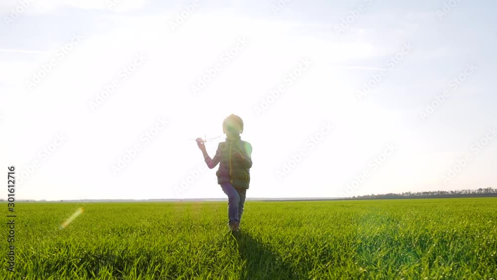 A little boy runs across the field, holding a toy plane in his hand. The child starts the plane. Emotions of the child: fun, happiness, smile. A little boy runs across the field, holding a toy plane in his hand. The child starts the plane. Emotions of the child: fun, happiness, smile.