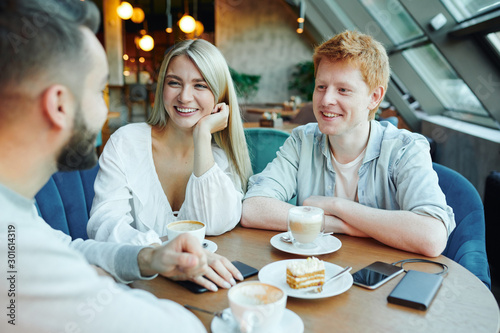 Happy young casual couple chatting to their friend by cup of coffee and dessert