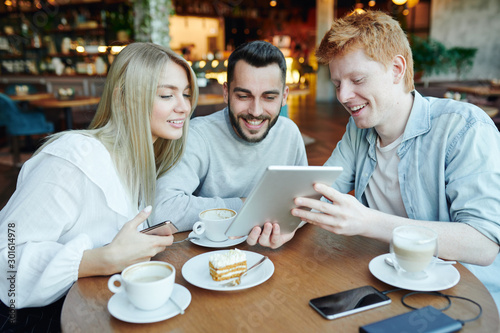 Cheerful man showing his friends curious video in tablet while relaxing in cafe