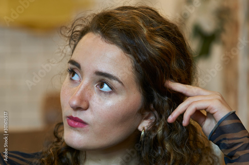 Pretty young brunette woman with curls and blonde highlights looking to the left while thinking