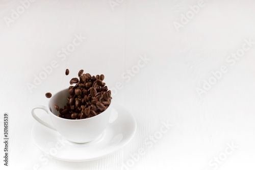 A cup with coffee beans in the air flying in flight like a spray. On background of a white wooden table  coffee shop advertising concept  copy space.