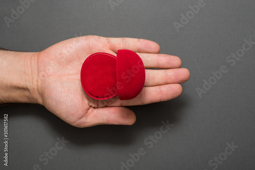 Empty open red jewelry box in male palm. Present. Black background. Top view