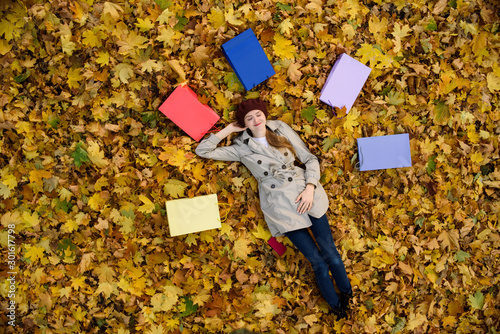 Happy young woman lies with her eyes closed, surrounded by colored packets on the foliage. Shopping View from above photo