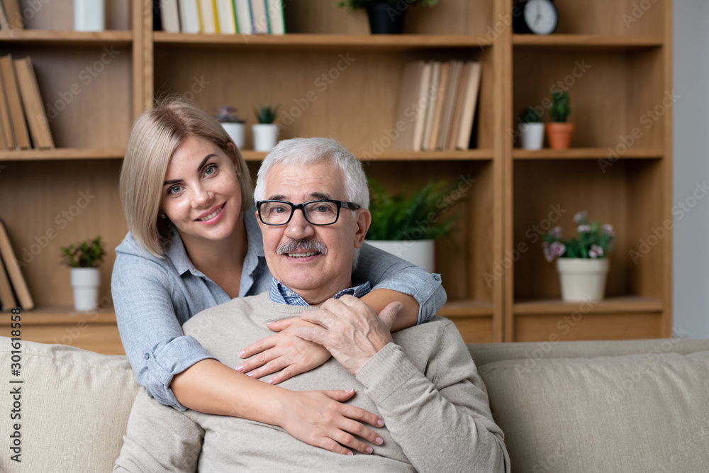 Happy blonde young woman embracing her cheerful senior father on couch Happy blonde young woman embracing her cheerful senior father on couch