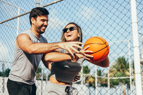 Summer vacation, sport, games and friendship concept - happy couple playing basketball outdoors
