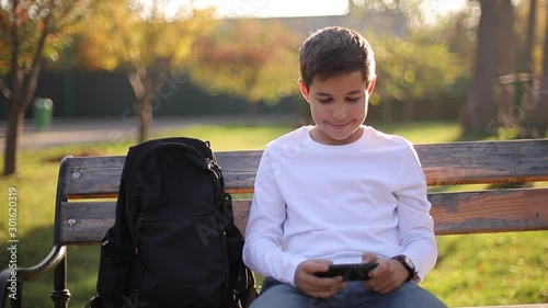 Teenage boy play online games on his smartphone in the park after lessons in school