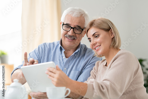 Senior grey-haired man and his pretty daughter watching online video in tablet