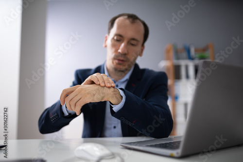 Businessman Holding Painful Wrist At Office Desk