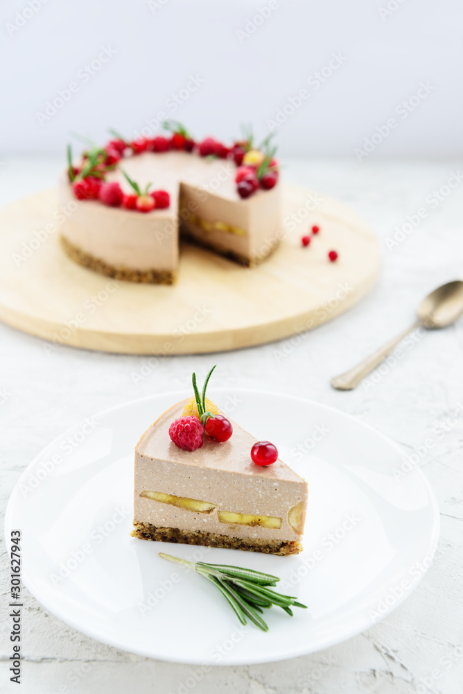Slice of raw cheesecake with cocoa, banana and berries on a white plate. Slice of raw cheesecake with cocoa, banana and berries on a white plate.