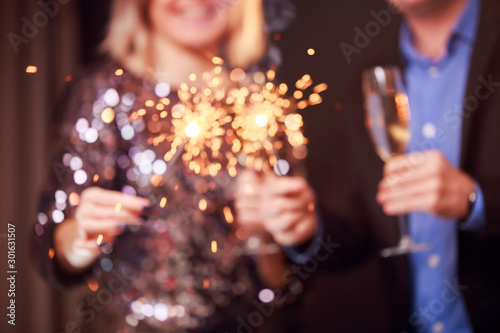 Photo of happy couple with champagne glasses and sparklers on black background