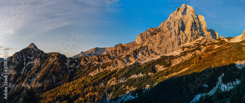 Fantastic view of a alpine mountain landscape of Totes Gebirge and the summit of Spitzmauer. Big rock wall, blue sky and mountains lid with orange sun. Sunrise or sunset mountain landscape, Austria. photo