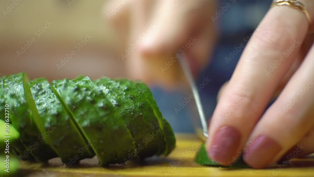Cutting fresh green cucumber on a wooden board in kitchen. female manicure. Cutting fresh green cucumber on a wooden board in kitchen. female manicure.