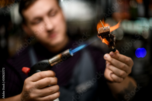 Bartender toasing a brownie pieces on the skewer with a burner
