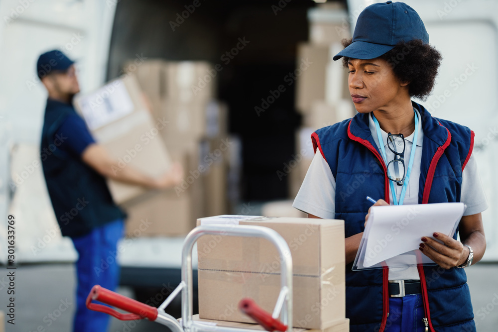 Obraz premium African American female worker writing data in a delivery list.