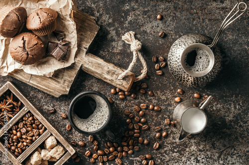 Coffee beans with coffee and muffins on dark textured background.
