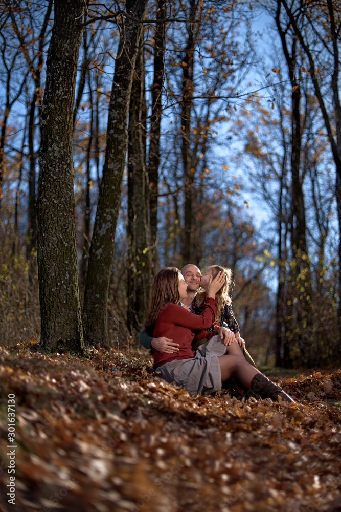 Young happy Parents with daughter among autumn leaves. Happy family resting in a beautiful autumn forest