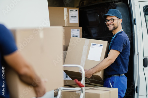 Happy delivery man talking with coworker while loading boxes in a truck. photo