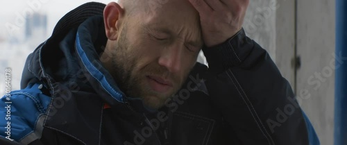 Tired caucasian worker or foreman in blue uniform takes off white helmet and wipes sweat from his forehead inside an unfinished building. Fatigue, feeling unwell, sadness, anamorphic shot
