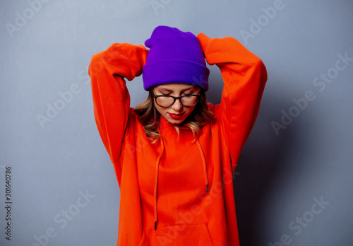 Style girl in orange hoodie and purple hat on grey background © Masson