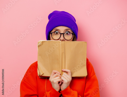 Style girl in orange hoodie and purple hat with book on pink background