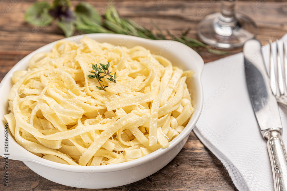 Homemade fettuccine with bechamel sauce in a white plate, rustic wooden table background, soft light - Italian food style