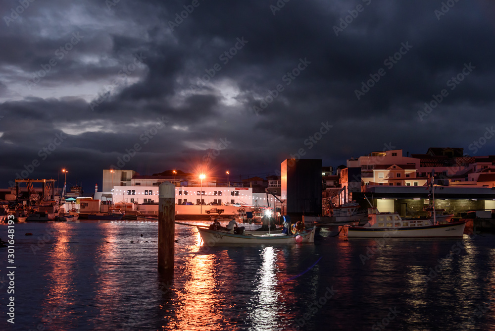 view of the port of sao mateus during night with streetlight reflection and boats. azores. portugal
