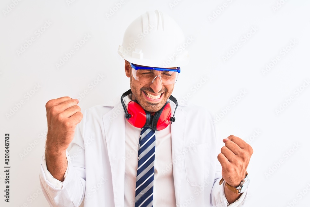Young chemist man wearing security helmet and headphones over isolated background very happy and excited doing winner gesture with arms raised, smiling and screaming for success. Celebration concept. Young chemist man wearing security helmet and headphones over isolated background very happy and excited doing winner gesture with arms raised, smiling and screaming for success. Celebration concept.