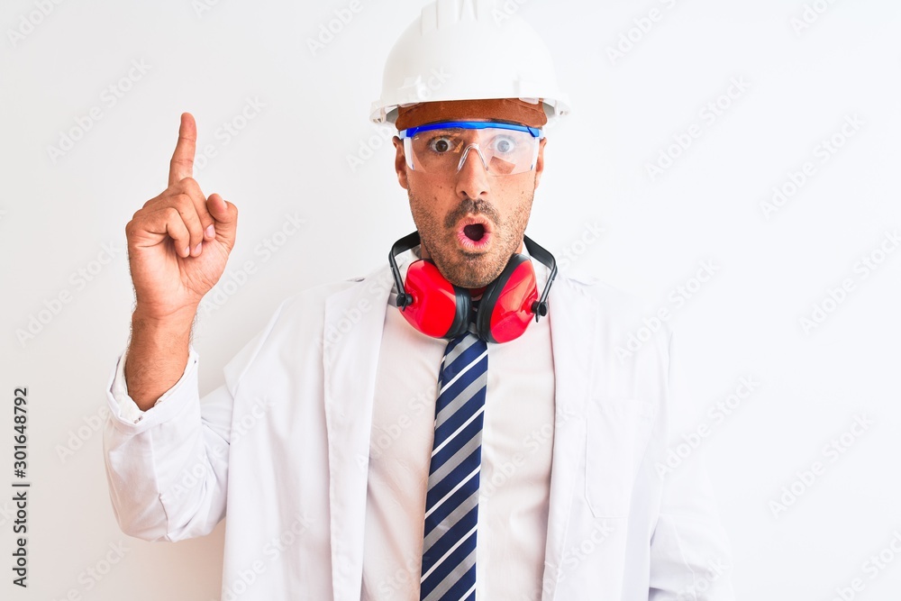 Young chemist man wearing security helmet and headphones over isolated background pointing finger up with successful idea. Exited and happy. Number one.