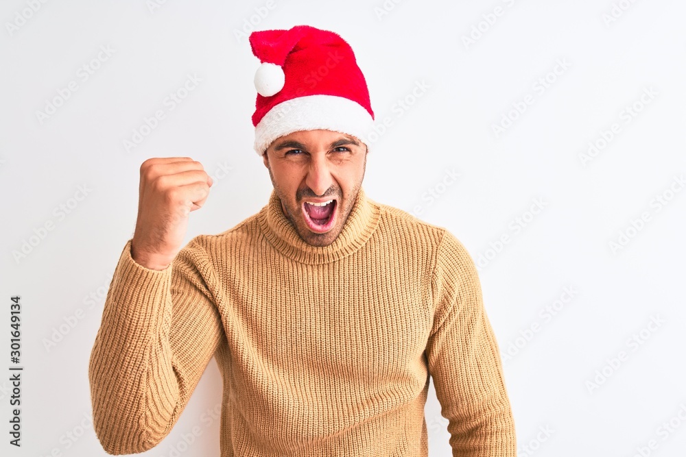 Young handsome man wearing christmas and turtleneck sweater over isolated background angry and mad raising fist frustrated and furious while shouting with anger. Rage and aggressive concept. Young handsome man wearing christmas and turtleneck sweater over isolated background angry and mad raising fist frustrated and furious while shouting with anger. Rage and aggressive concept.
