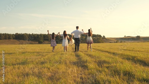 mother, father and little daughter with sisters walking in field in the sun. Happy young family. Children, dad and mom play in meadow in the sunshine. concept of happy family.