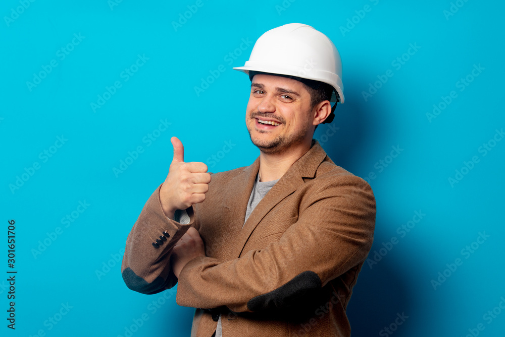 Young engineer in helmet and jacket on blue background Young engineer in helmet and jacket on blue background