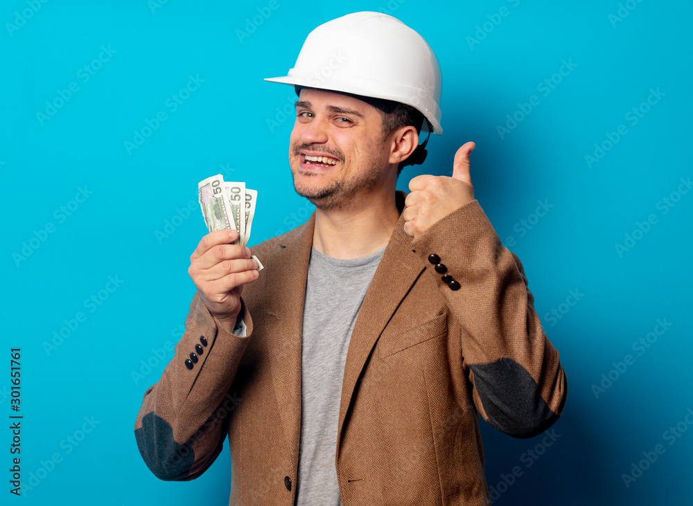 Young man in helmet with salary on blue background Young man in helmet with salary on blue background