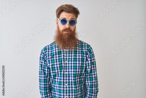 Young redhead irish man wearing casual shirt and sunglasses over isolated white background Relaxed with serious expression on face. Simple and natural looking at the camera.