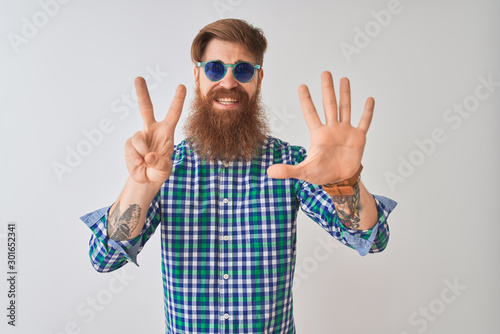 Young redhead irish man wearing casual shirt and sunglasses over isolated white background showing and pointing up with fingers number seven while smiling confident and happy.