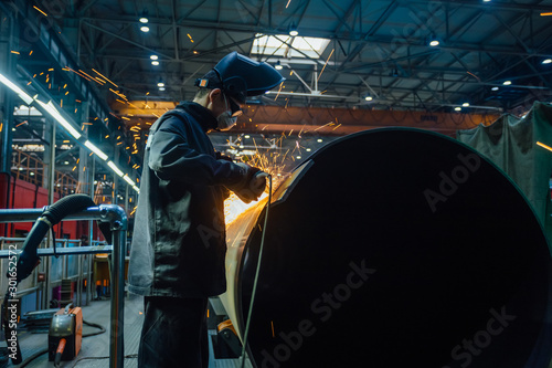 Worker in protective mask grinding pipe after welding