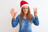 Young beautiful redhead woman wearing christmas hat over isolated background showing and pointing up with fingers number eight while smiling confident and happy.