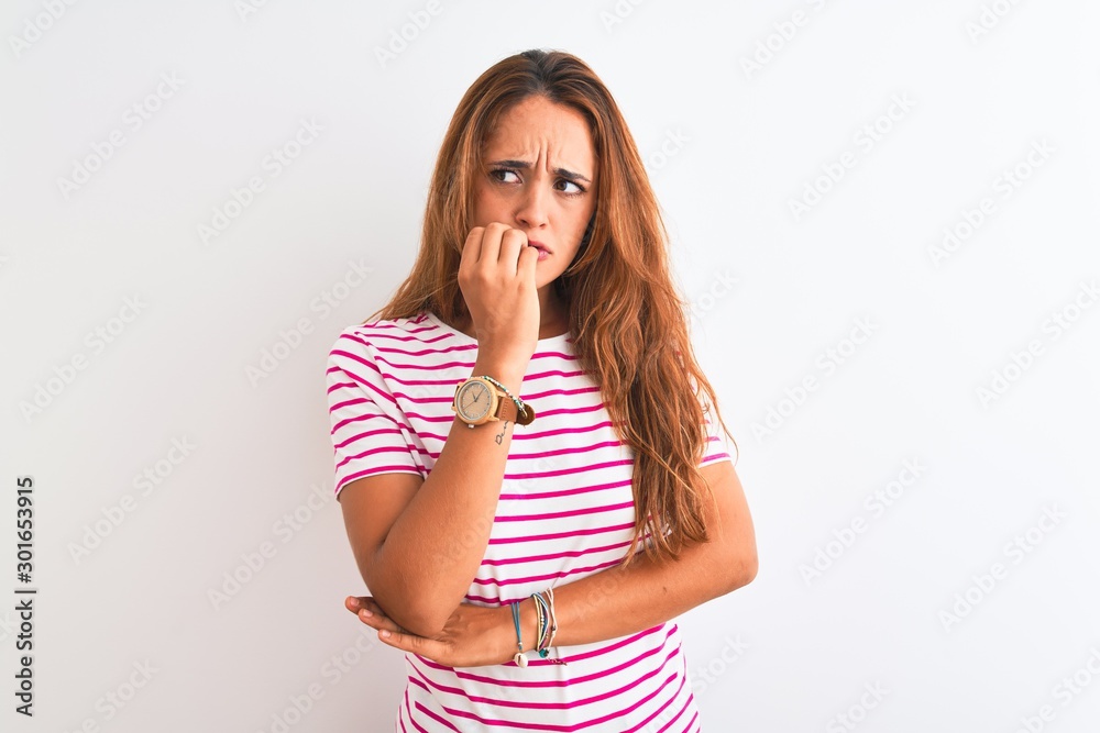 Young redhead woman wearing striped casual t-shirt stading over white isolated background looking stressed and nervous with hands on mouth biting nails. Anxiety problem. Young redhead woman wearing striped casual t-shirt stading over white isolated background looking stressed and nervous with hands on mouth biting nails. Anxiety problem.