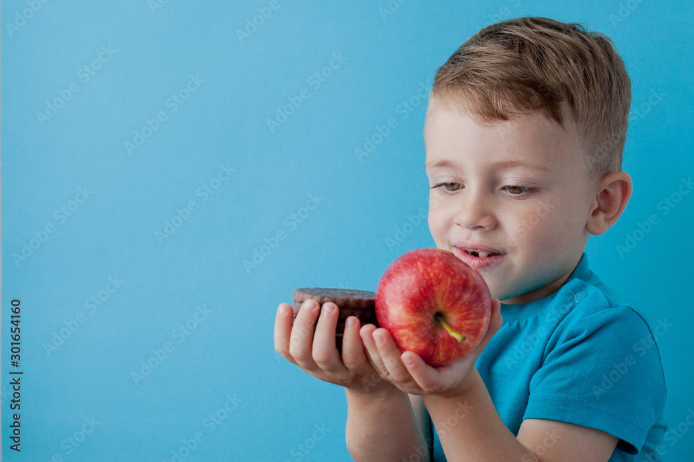 Portrait happy, smiling boy choosing junk food. Healthy versus unhealthy food. Healthy vs unhealthy eating, teenager choosing between cookie or an apple Portrait happy, smiling boy choosing junk food. Healthy versus unhealthy food. Healthy vs unhealthy eating, teenager choosing between cookie or an apple