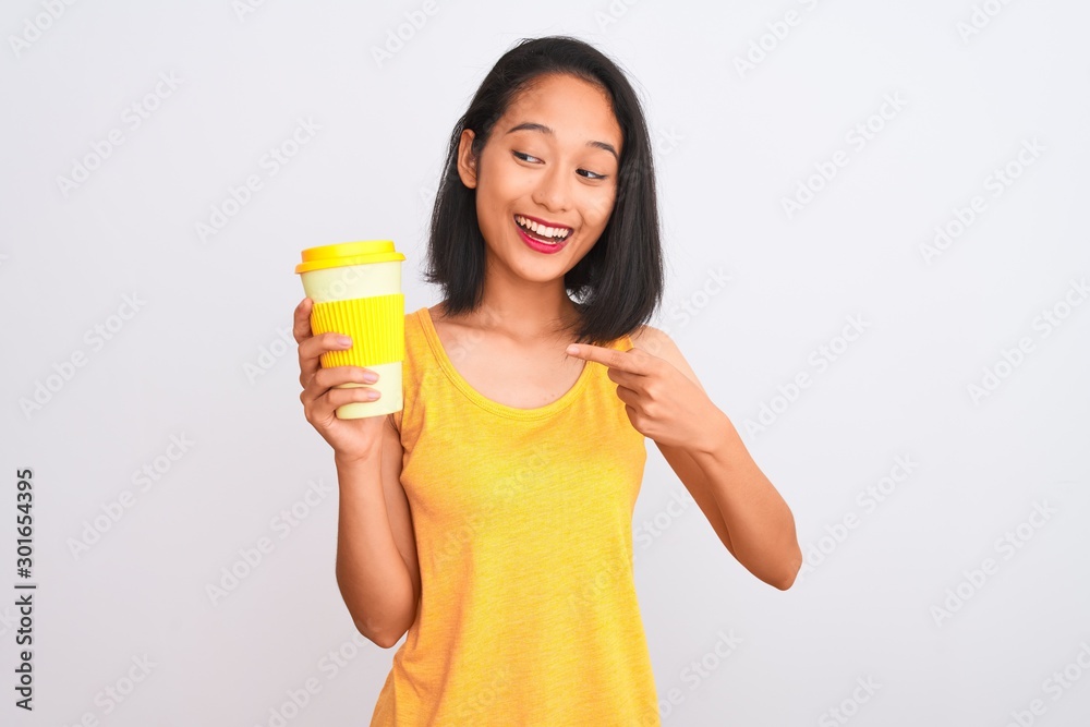 Young chinese woman drinking take away glass of coffee over isolated white background very happy pointing with hand and finger Young chinese woman drinking take away glass of coffee over isolated white background very happy pointing with hand and finger