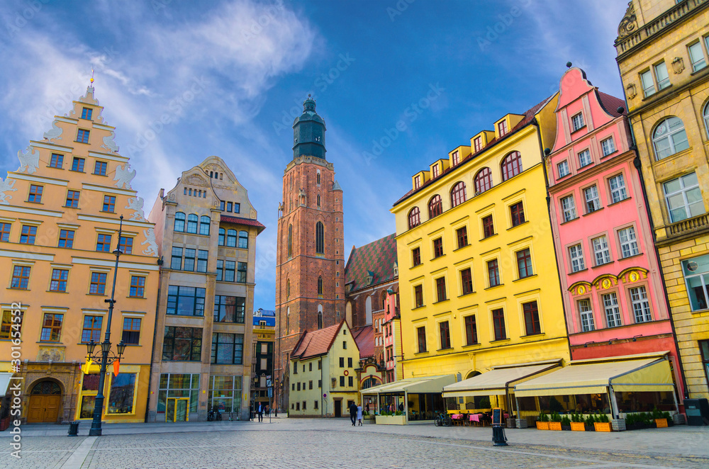 Row of colorful buildings with multicolored facade and St. Elizabeth Minor Basilica Garrison catholic Church on cobblestone Rynek Market Square in old town historical city centre of Wroclaw, Poland