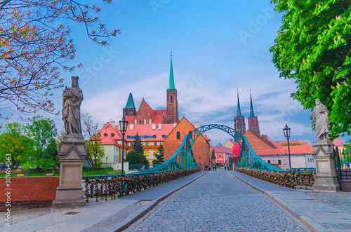 Cobblestone road and Tumski bridge over Odra Oder river, Collegiate Church of Holy Cross and Cathedral of St. John the Baptist in old historical city centre of Wroclaw, evening view, Poland