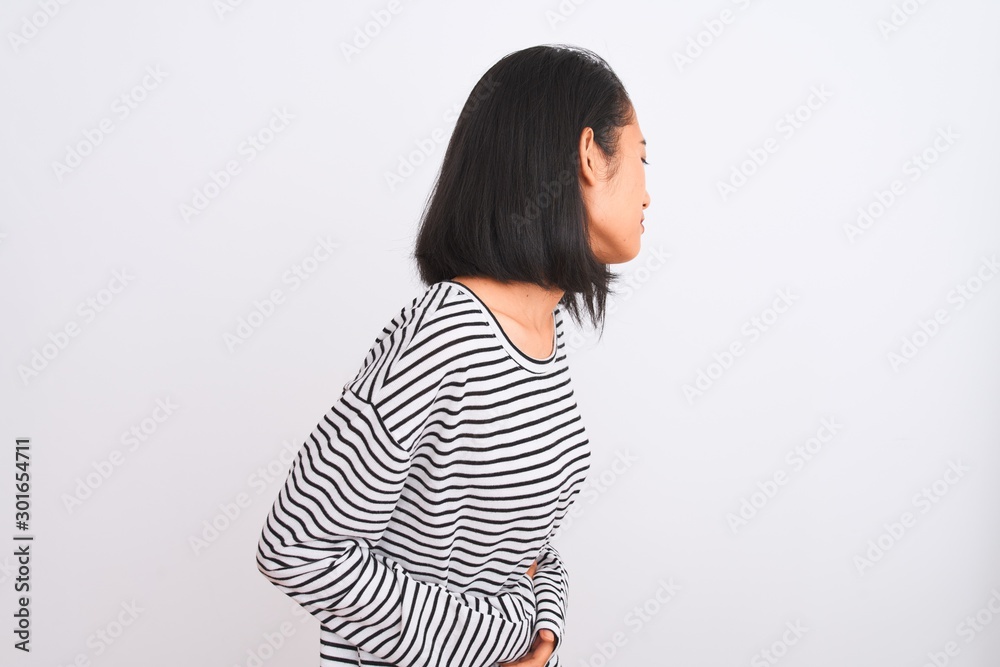 Young chinese woman wearing striped t-shirt standing over isolated white background with hand on stomach because nausea, painful disease feeling unwell. Ache concept. Young chinese woman wearing striped t-shirt standing over isolated white background with hand on stomach because nausea, painful disease feeling unwell. Ache concept.