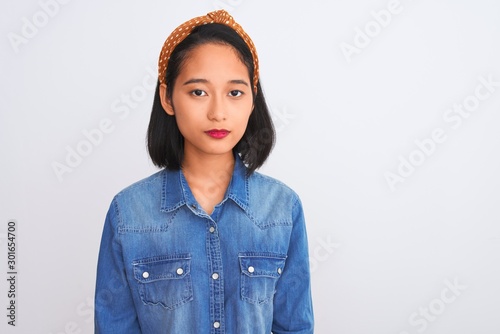 Obraz na plátně Young beautiful chinese woman wearing denim shirt standing over isolated white background with serious expression on face