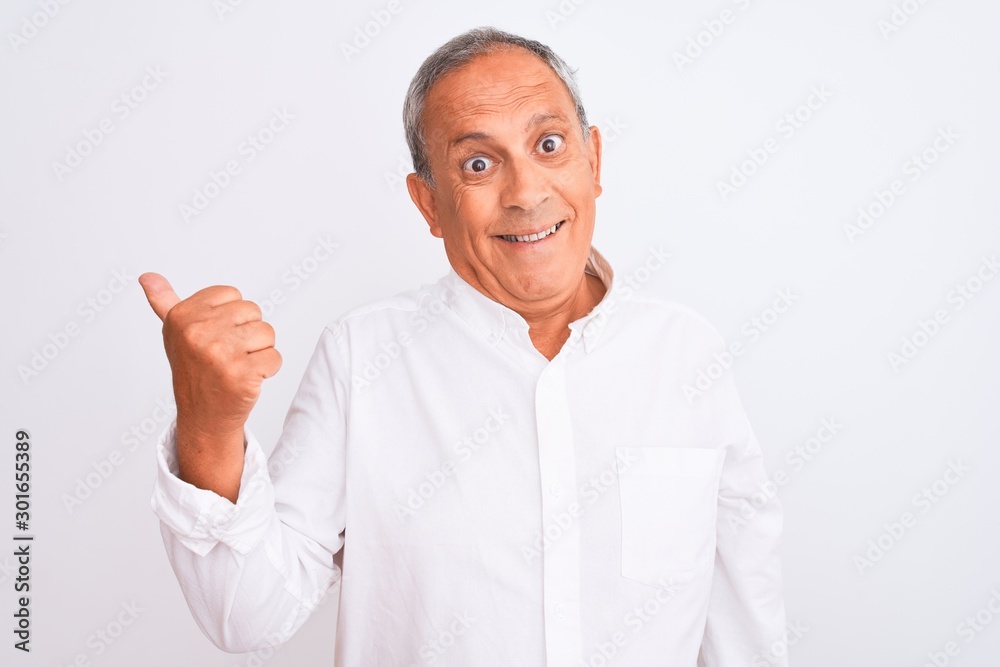 Senior grey-haired man wearing elegant shirt standing over isolated white background smiling with happy face looking and pointing to the side with thumb up. Senior grey-haired man wearing elegant shirt standing over isolated white background smiling with happy face looking and pointing to the side with thumb up.