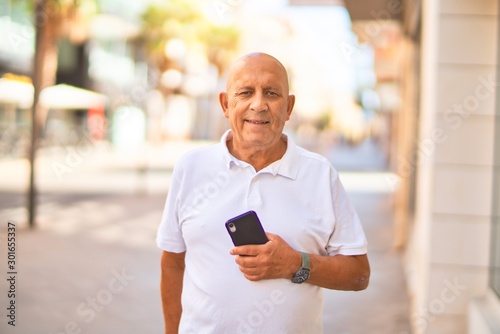 Senior handsome man smiling happy and confident. Standing with smile on face using smartphone at town street