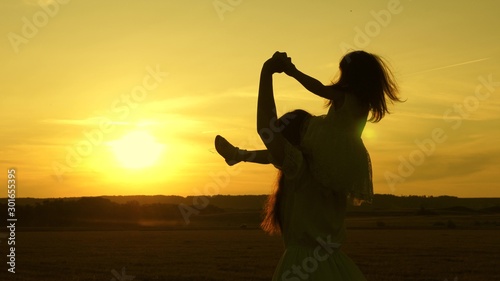 Happy mom and baby walk across the field at sunset and laugh. A little girl sits on her mother shoulders and walks together in the park in the sun and smiles. Family life concept. Slow motion.