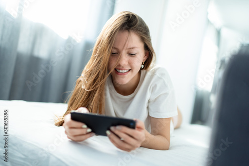 Adorable teen having fun in a bed, while video communicating with a smartphone.
