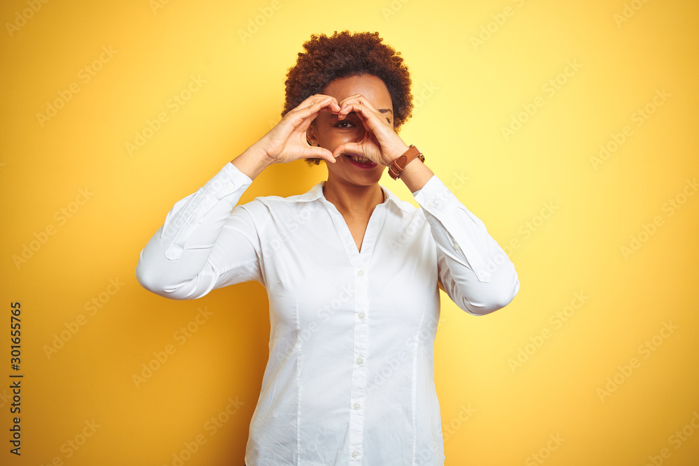 African american business woman over isolated yellow background Doing heart shape with hand and fingers smiling looking through sign