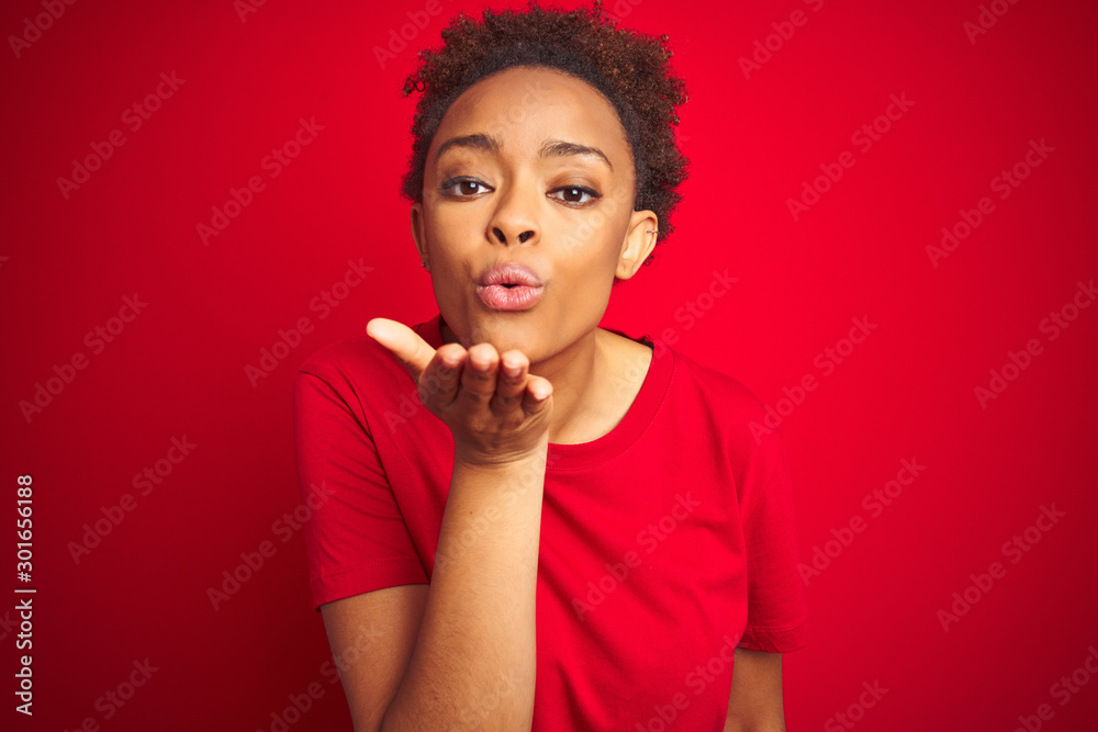 Young beautiful african american woman with afro hair over isolated red background looking at the camera blowing a kiss with hand on air being lovely and sexy. Love expression. Young beautiful african american woman with afro hair over isolated red background looking at the camera blowing a kiss with hand on air being lovely and sexy. Love expression.
